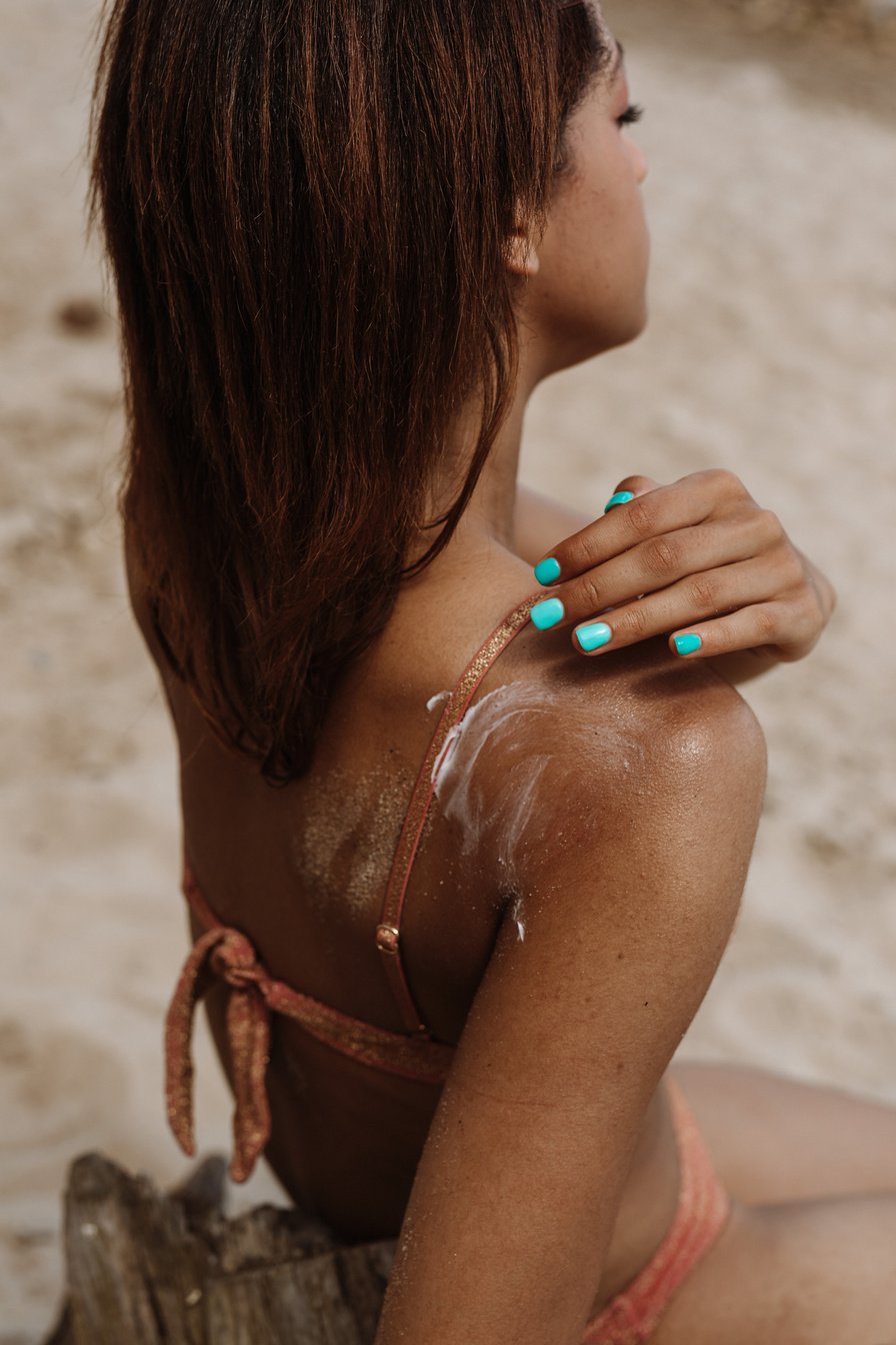 a person in a bikini sitting spreading sunblock on their shoulders